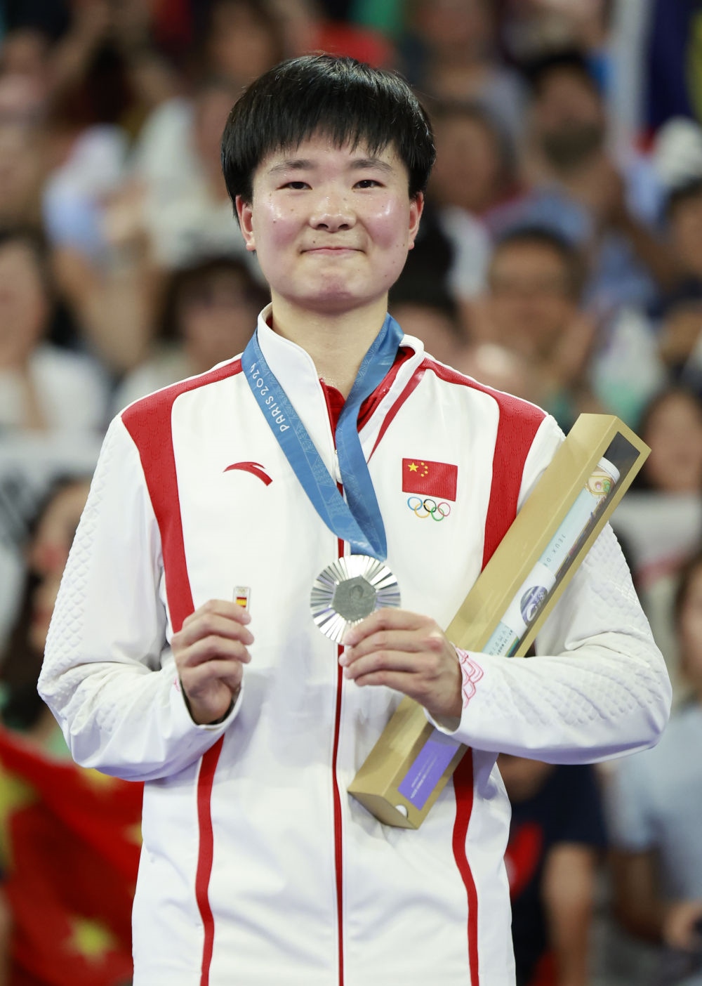 巴黎奧運(yùn)會(huì)羽毛球女子單打亞軍、中國(guó)選手何冰嬌在頒獎(jiǎng)儀式上一手握著銀牌，一手握著西班牙奧委會(huì)徽章（2024年8月5日攝）。新華社記者 任正來(lái) 攝